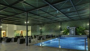 Une piscine intérieure dotée d’un toit en verre, entourée de tables et de chaises, et un petit coin salon agrémenté de plantes.