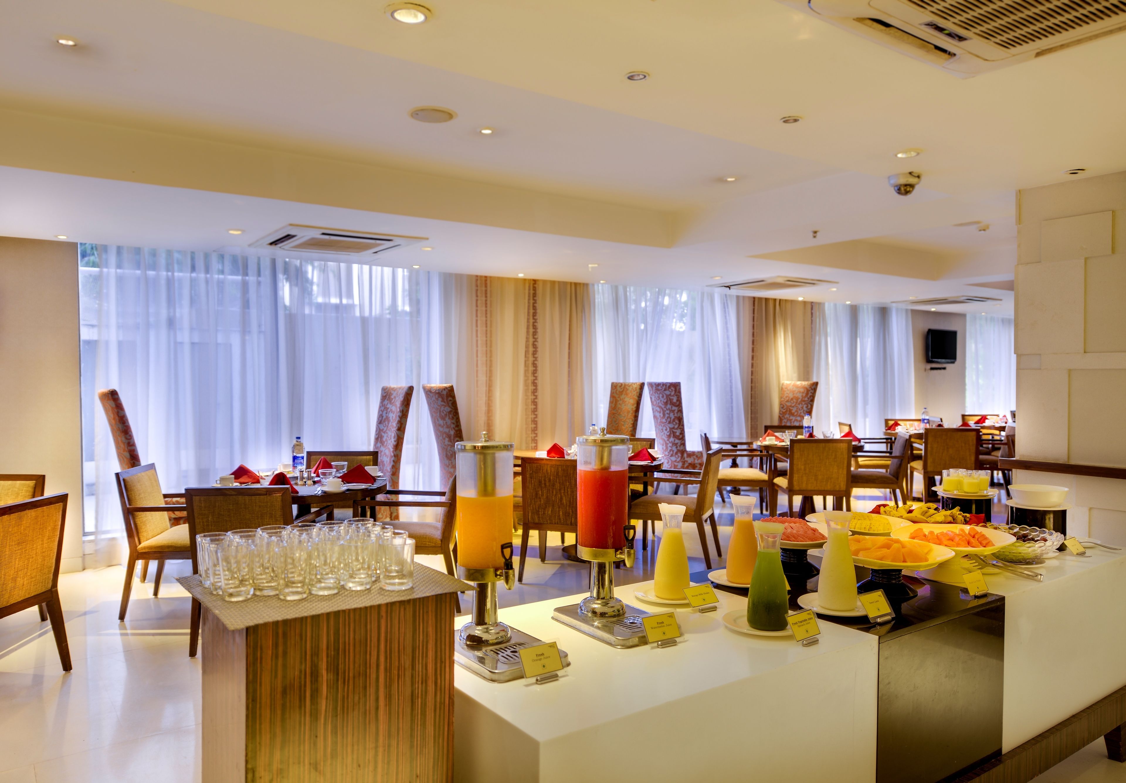A hotel dining area with multiple tables, chairs, and a buffet with various food items and drinks.