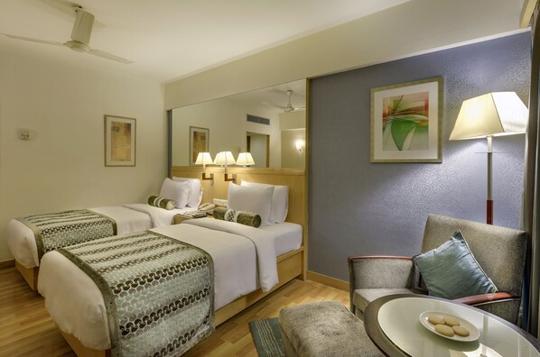 A hotel room with two beds, a sitting area with a chair and a table, a large mirror, and a painting on the wall.