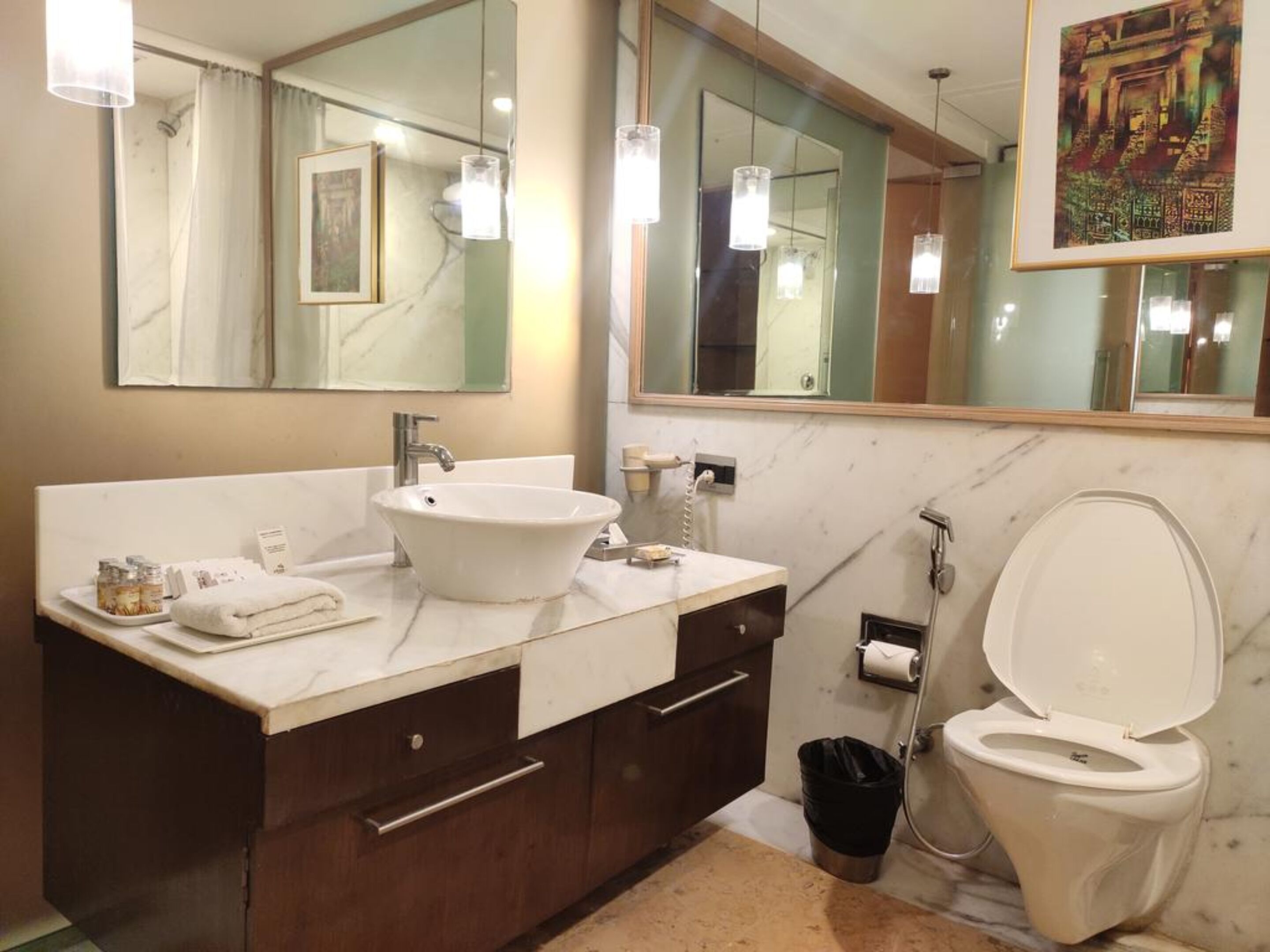 A bathroom with a white sink, mirror, and toilet. There are cabinets, a towel, and a trash can.