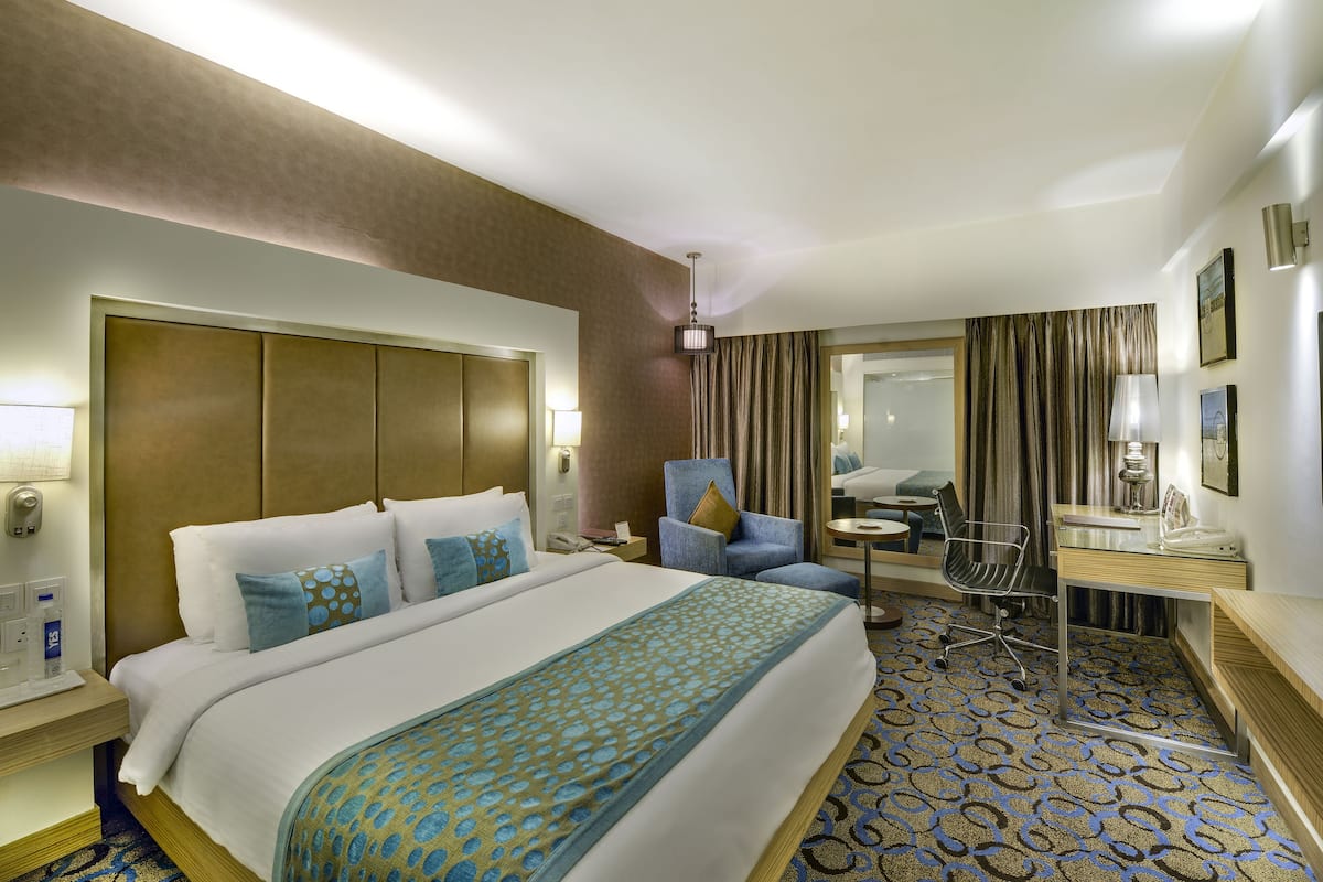 A hotel room with a large bed, a desk, a chair, a mirror, and a television.
