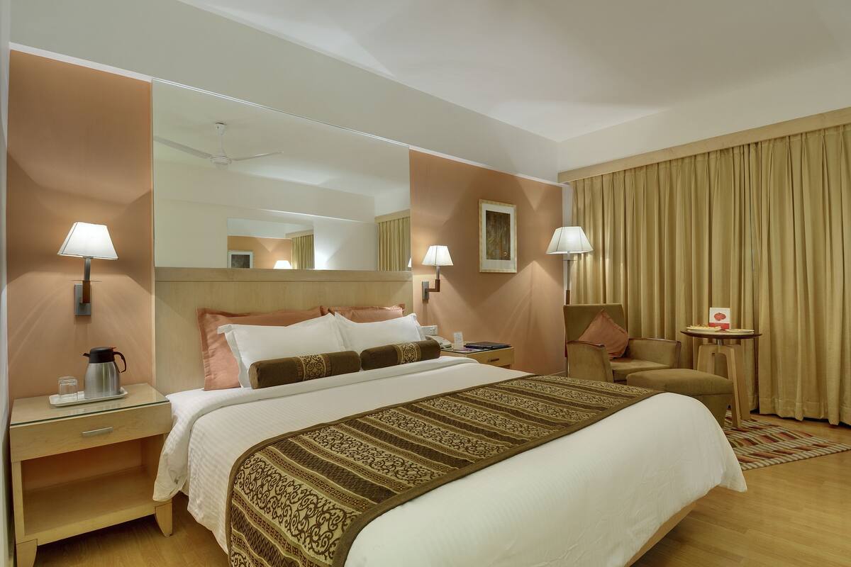A hotel room with a large bed, two bedside tables, a chair, a small table, and a mirror.