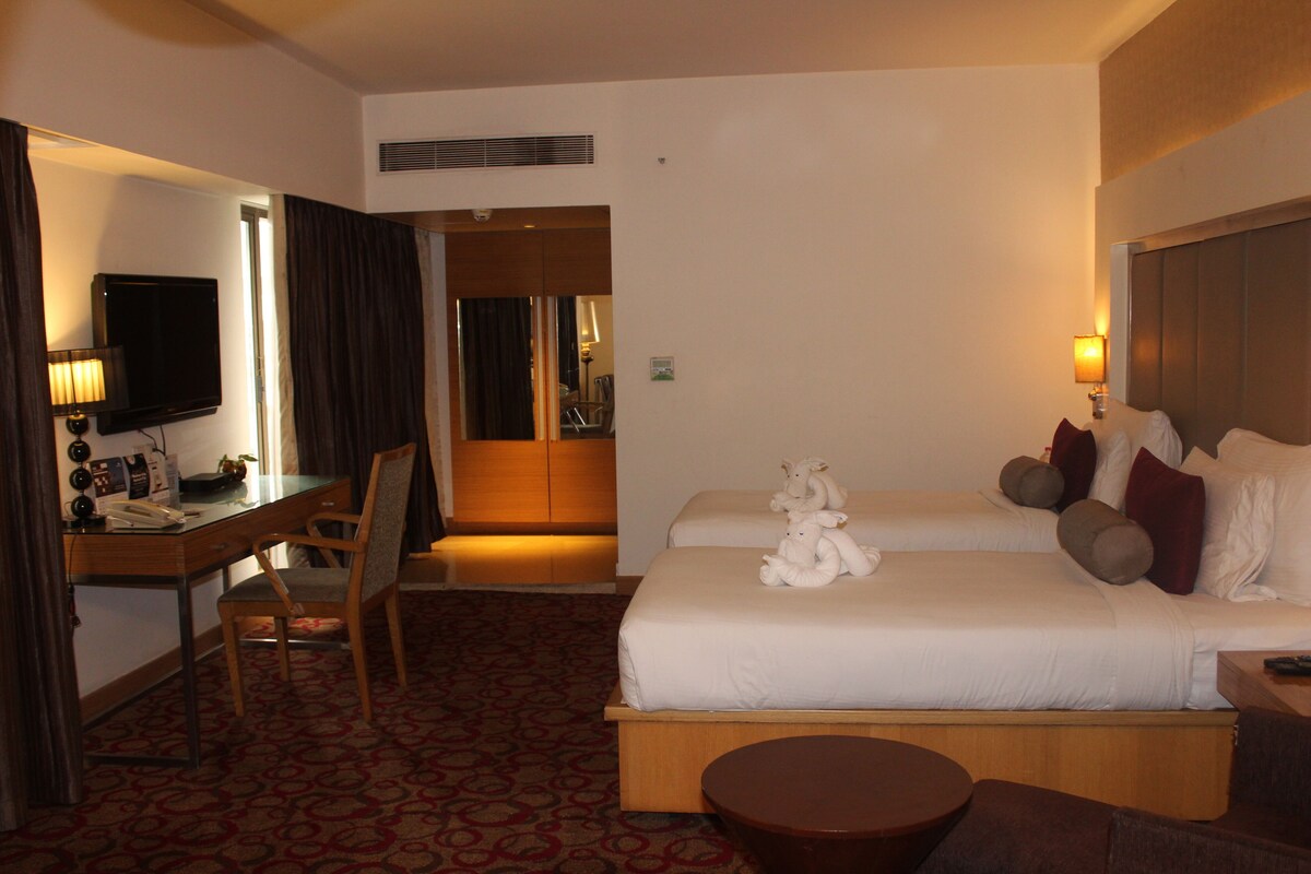 A hotel room with a bed, a desk, a chair, a television, and a lamp.
