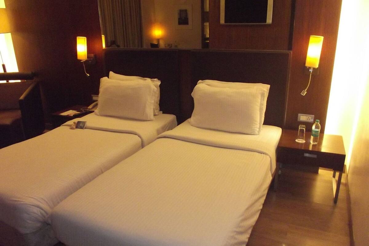 A hotel room with two single beds, a nightstand with a lamp, a chair, and a desk with a phone.