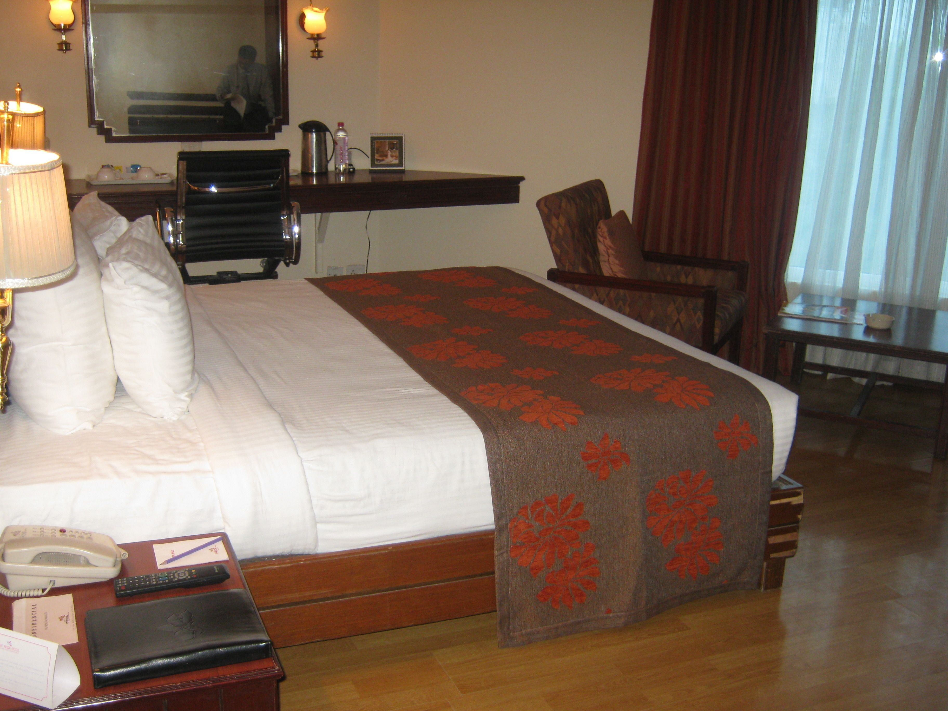 Une chambre d’hôtel équipée d’un lit, d’un bureau, d’une chaise, d’une lampe, d’un téléphone et d’un miroir.