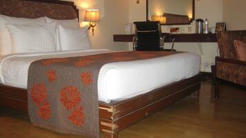 Quarto de hotel com uma cama grande, uma mesa com cadeira, um espelho e luminárias na parede.