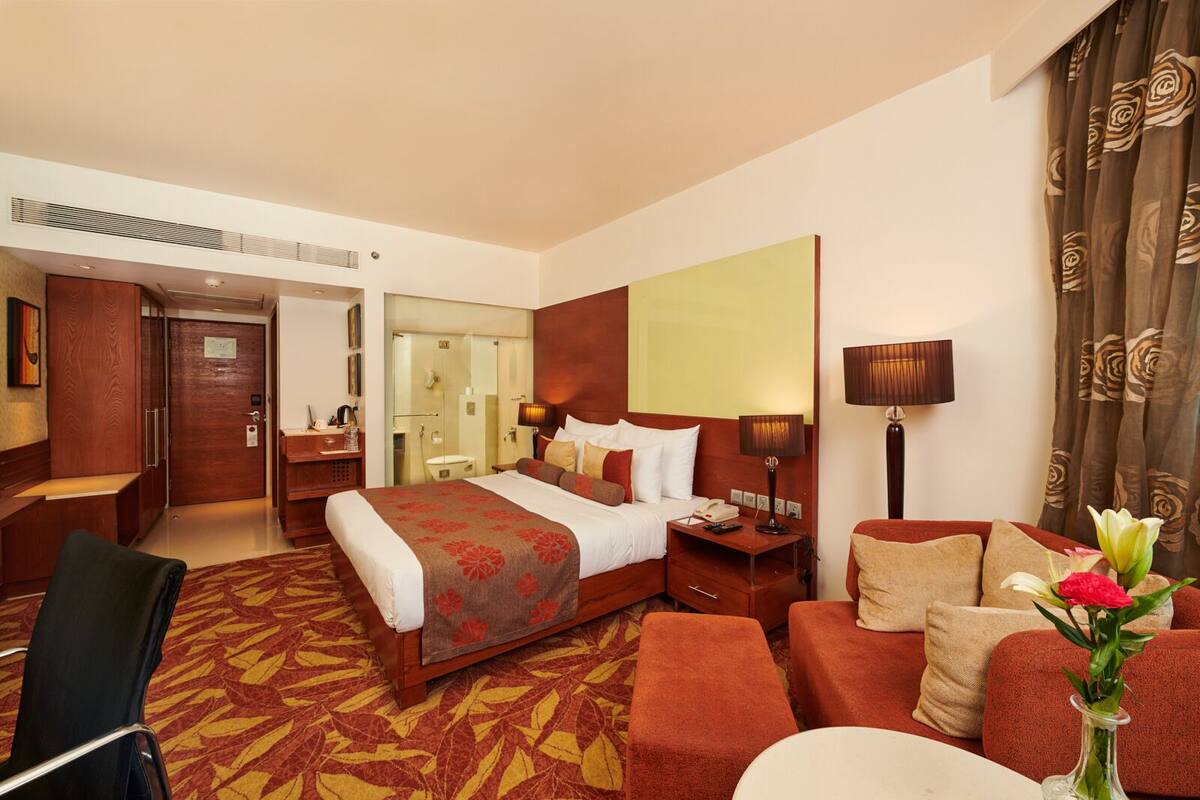 Ein Hotelzimmer mit einem großen Bett, einem Schreibtisch, einem Sessel, einer Couch und einem durchgegangenen Tür erkennbaren Badezimmer.