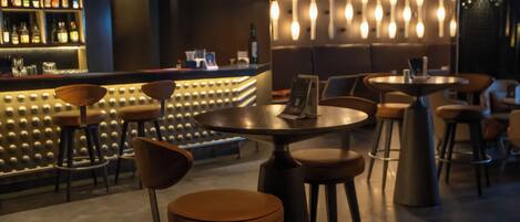 A bar area with stools, tables, and a bar counter with bottles.