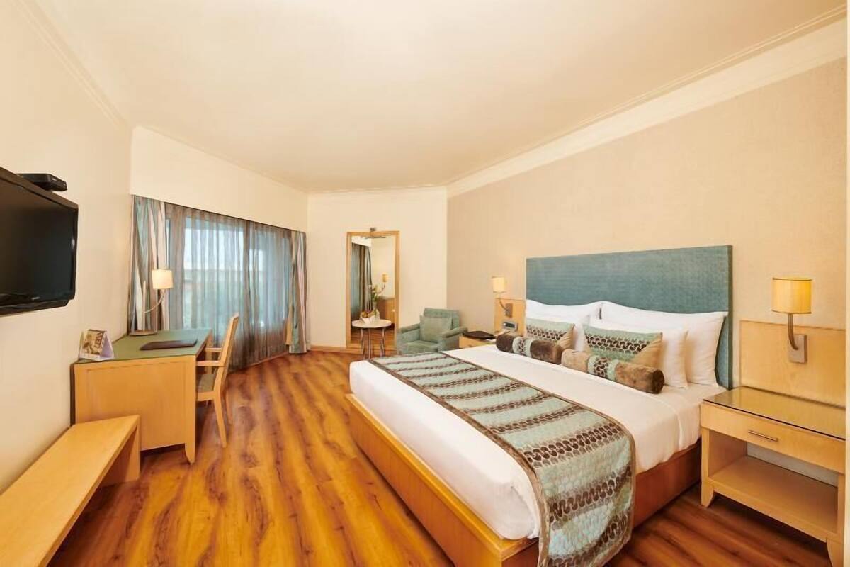Ein Hotelzimmer mit Bett, Schreibtisch, Stuhl, Nachttischen, Lampen und einem Fernseher.