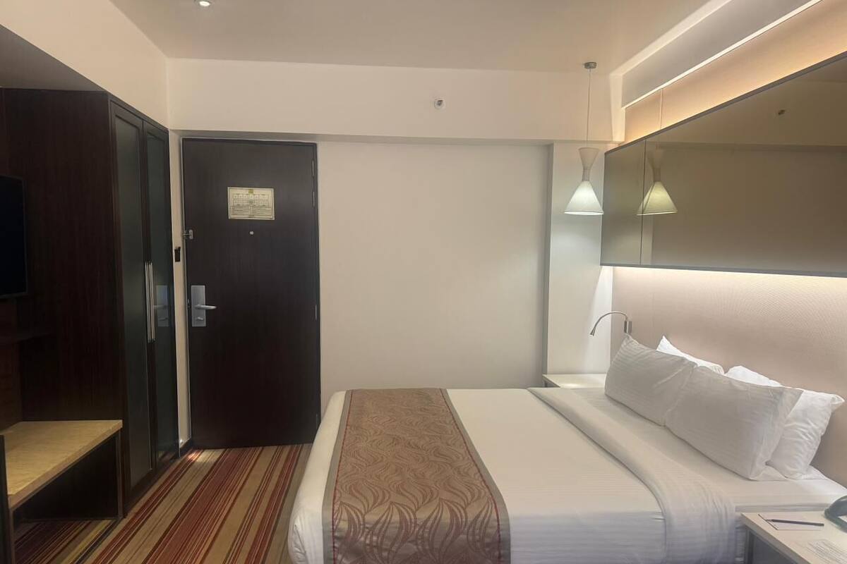 Una habitación de hotel con cama, mesita de noche, lámpara y una puerta con un cartel.