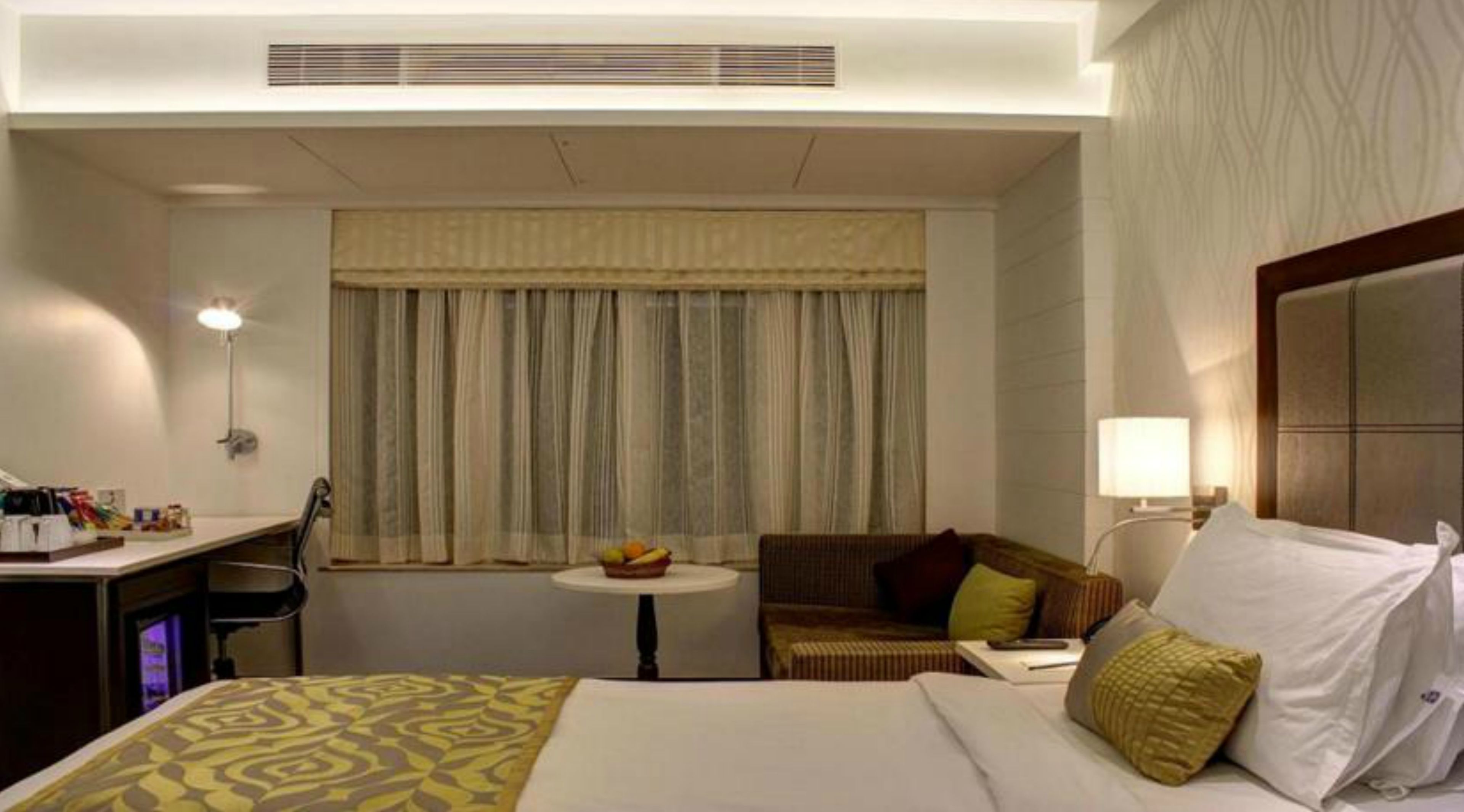 A hotel room with a bed, a desk, a chair, a small table with fruit, and a sofa.