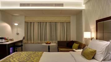 A hotel room with a bed, a desk, a chair, a small table with fruit, and a sofa.