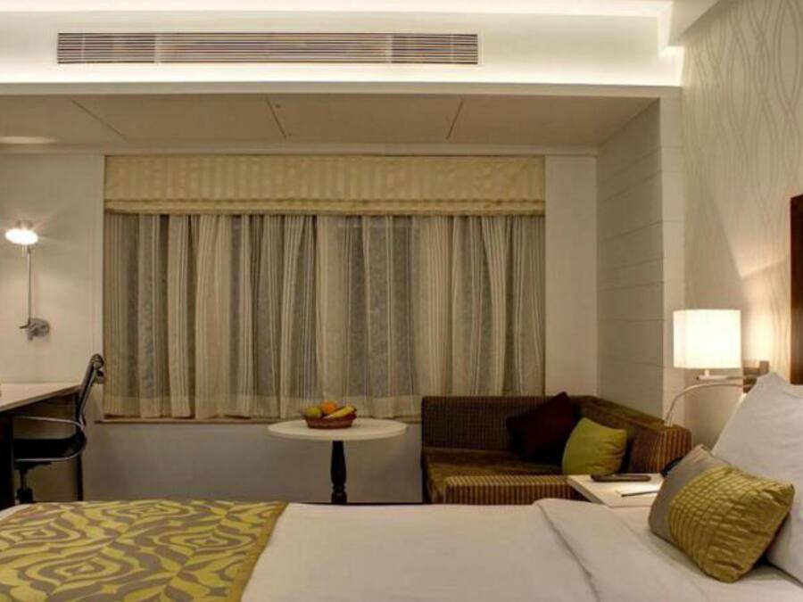 A hotel room with a bed, a desk, a chair, a small table with fruit, and a sofa.
