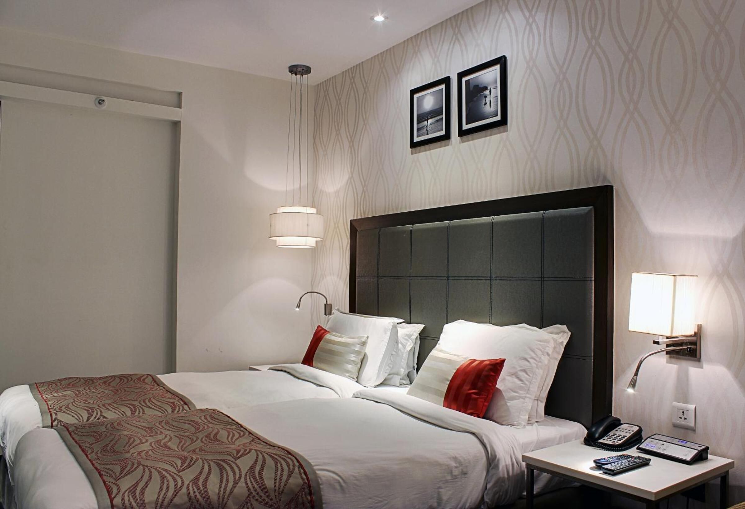 Ein Hotelzimmer mit einem großen Bett, einem Nachttisch mit Telefon und Bedienfeld, einer Wandlampe sowie zwei gerahmten Bildern an der Wand.