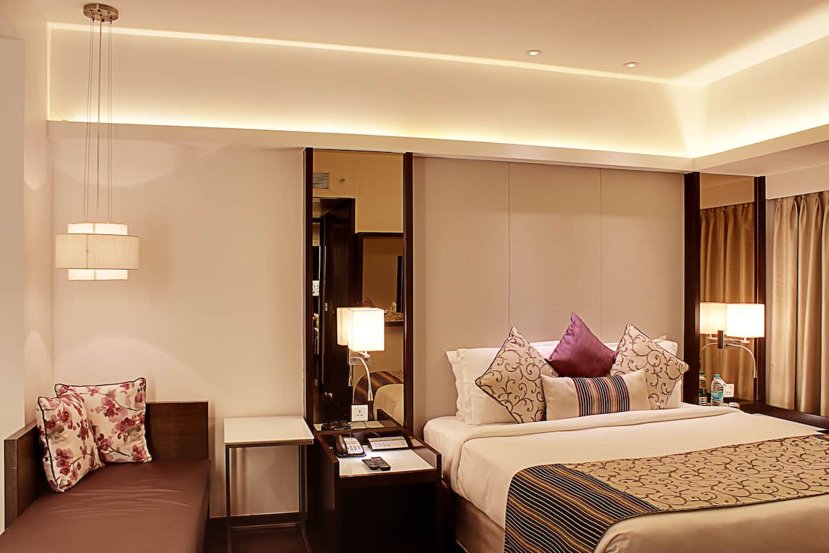 Habitación de hotel con cama, mesitas de noche, espejo y lámpara colgante.