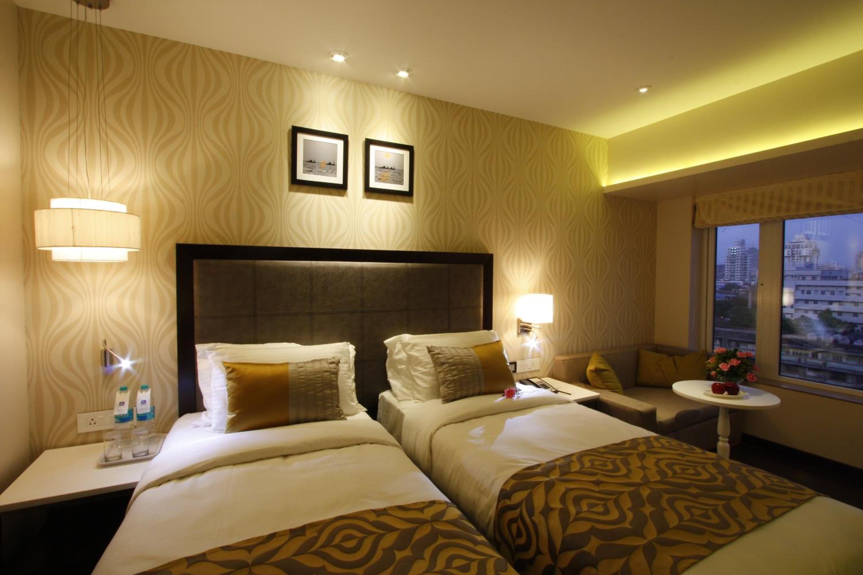 A hotel room with two beds, a sofa, a small table, and a window with a city view.