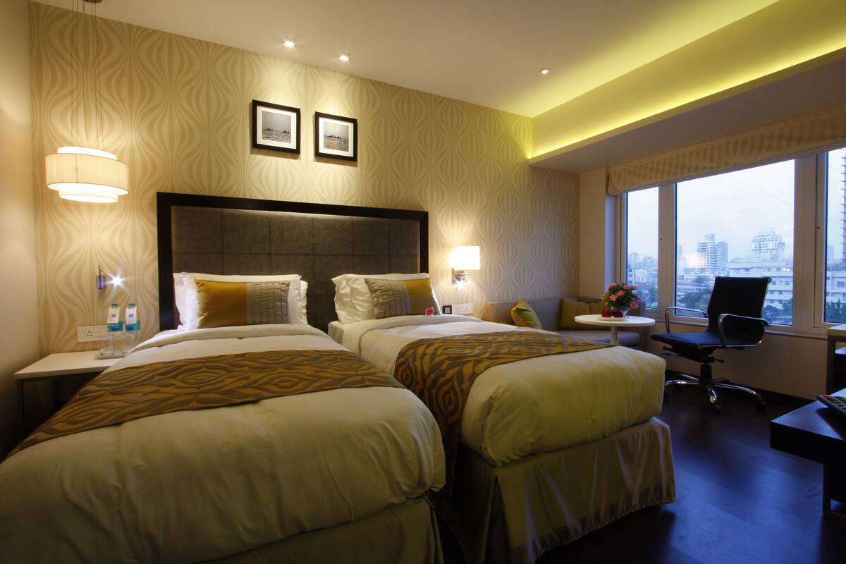 Habitación de hotel con dos camas, un escritorio, una silla y vista a la ciudad.
