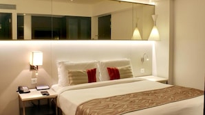 A hotel room with a large bed, a bedside table with a phone and a lamp, and a mirror above the bed. - The Sahil Hotel (Mumbai)