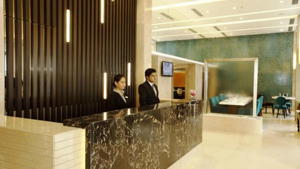 A hotel reception area with a marble counter, a reception desk, and a seating area with tables and chairs. - The Sahil Hotel (Mumbai)
