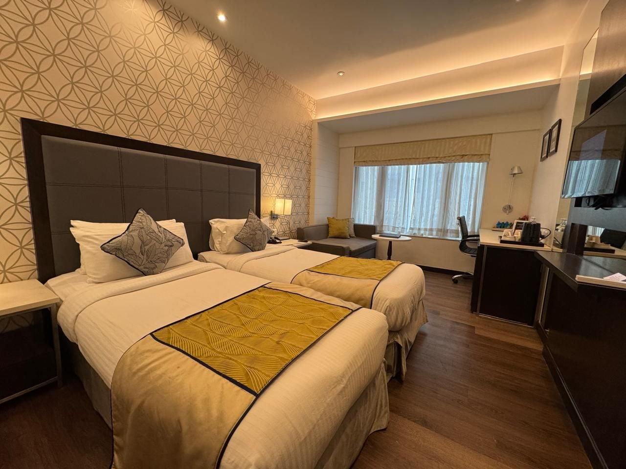 Una habitación de hotel con dos camas, un escritorio, una silla y una ventana con cortinas.