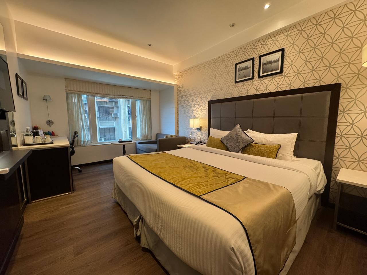 Habitación de hotel con una cama grande, mesitas de noche, un escritorio y una ventana con cortinas.