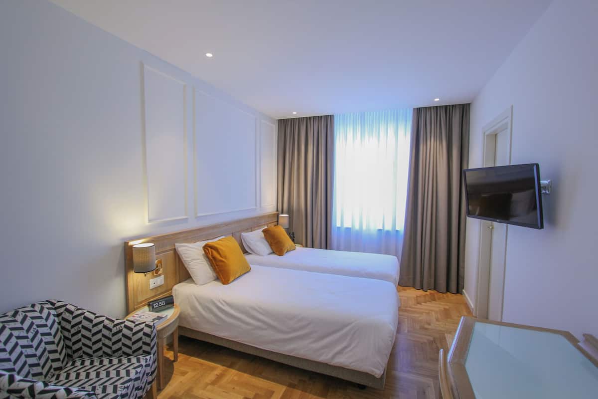 Habitación de hotel con dos camas, un televisor, una silla y una mesita de noche con lámpara.