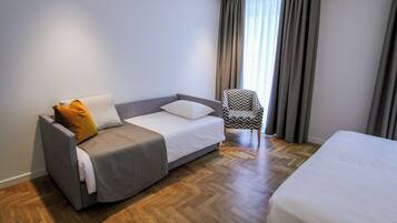 Una camera d'albergo moderna con un divano grigio, una poltrona a fantasia e un letto grande.