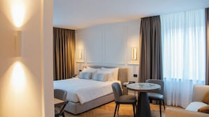 A hotel room with a bed, a desk, a chair, a sofa, and a window with curtains. - Ambassador Palace Hotel (Udine)