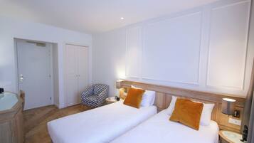 A hotel room with two beds, a desk with a chair, a small table, and a wall-mounted lamp.