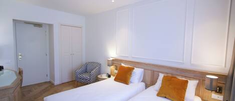 A hotel room with two beds, a desk with a chair, a small table, and a wall-mounted lamp.