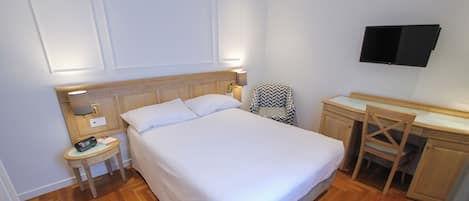Un dormitorio ordenado con una cama grande, mesita de noche, silla, escritorio y un televisor de pantalla plana montado en la pared.