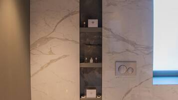Ein modernes Badezimmer mit integriertem Bidet, Toilette, Marmorwänden und Ablage für Toilettenartikel.