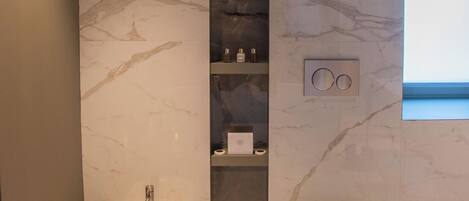 A modern bathroom with a bidet, toilet, marble walls, and a shelf with toiletries.