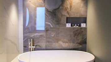 Un baño moderno con una bañera independiente, paredes de mármol y estantes empotrados.