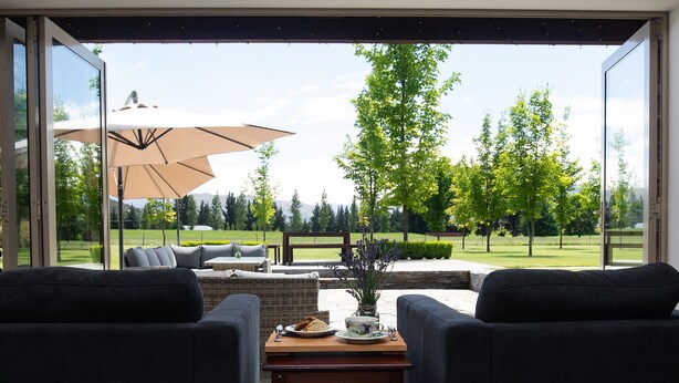 Un moderno salón con un gran ventanal que da a un patio con mobiliario exterior y vistas a un campo de golf.