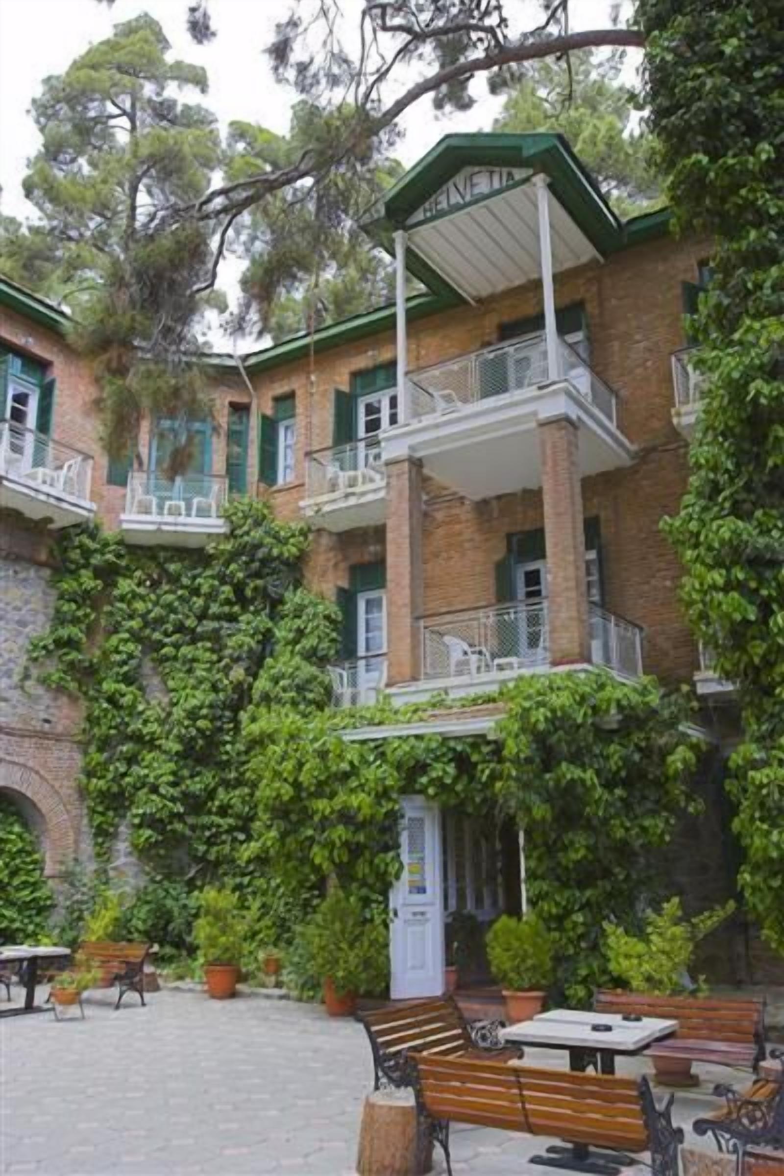 A courtyard with outdoor seating, a covered balcony, and a brick building with green shutters.