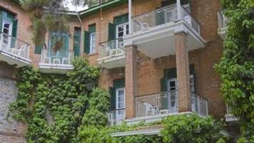 A courtyard with outdoor seating, a covered balcony, and a brick building with green shutters.