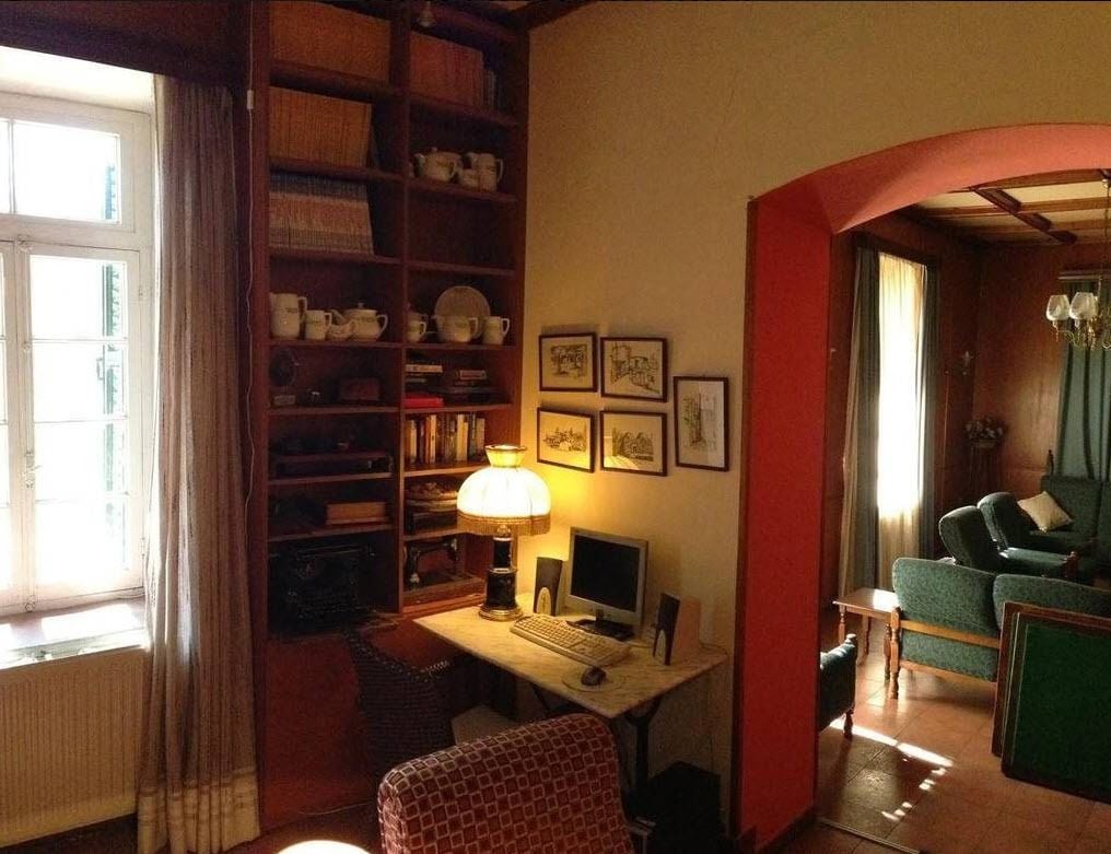 Una camera accogliente con una libreria in legno, una scrivania con un computer e una poltrona verde.