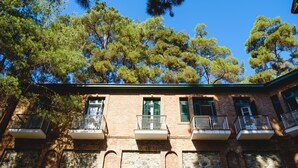 Un edificio de dos pisos con fachada de ladrillo, contraventanas verdes y balcones con barandillas de metal.