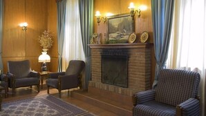 Una sala de estar acogedora con chimenea, dos sillones, una mesita de noche con lámpara y un espejo decorativo sobre la chimenea.
