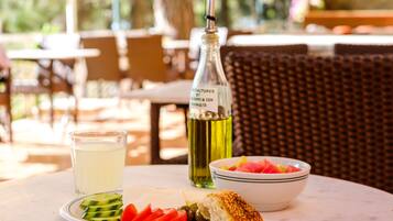 A table with a plate of sliced vegetables, a bowl of fruit, a bottle of olive oil, and a glass of water.