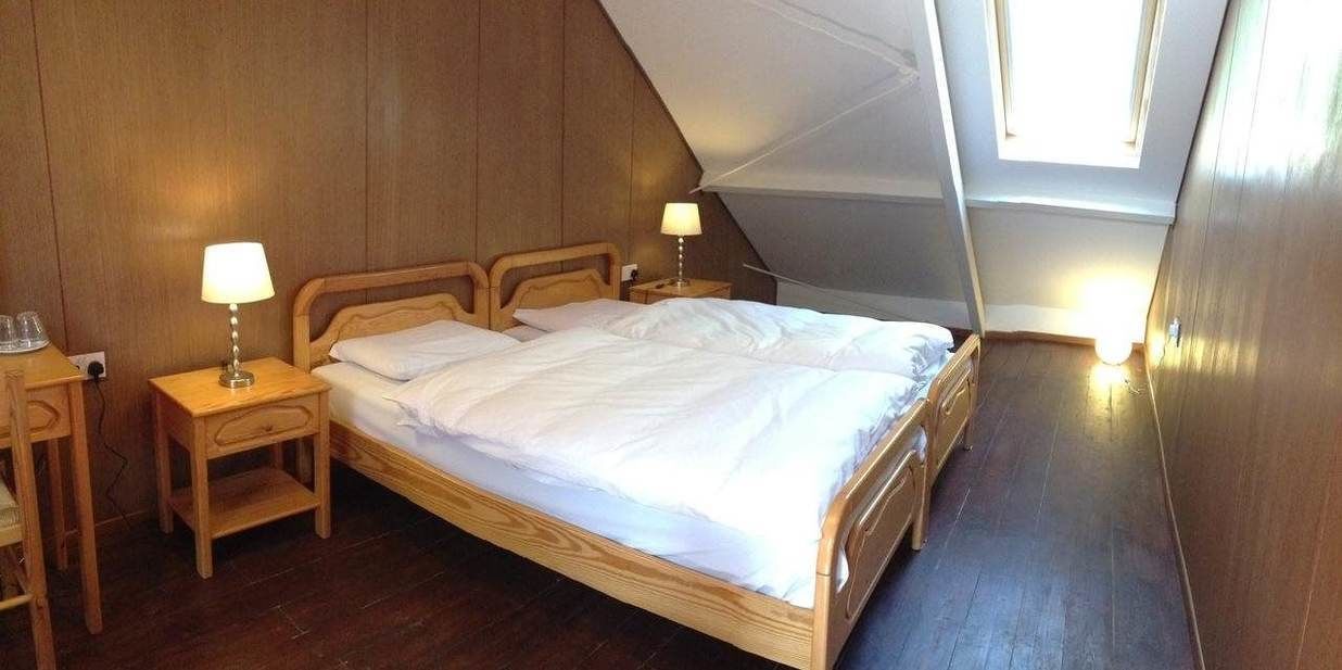 A single bed with a wooden headboard, two bedside tables with lamps, and a sloped ceiling with a skylight.
