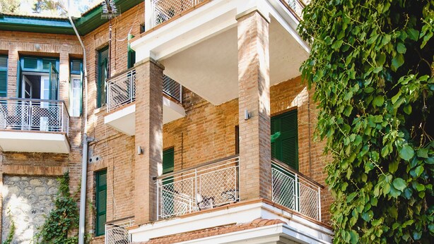 Un patio con un banco, plantas en macetas y un edificio con fachada de piedra y balcones.