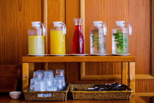 A wooden table with four glass pitchers of different beverages and two wicker baskets filled with clear plastic cups.