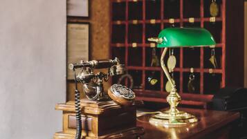 A vintage telephone with a green desk lamp, a wooden box, and a wall with a grid of bottles.