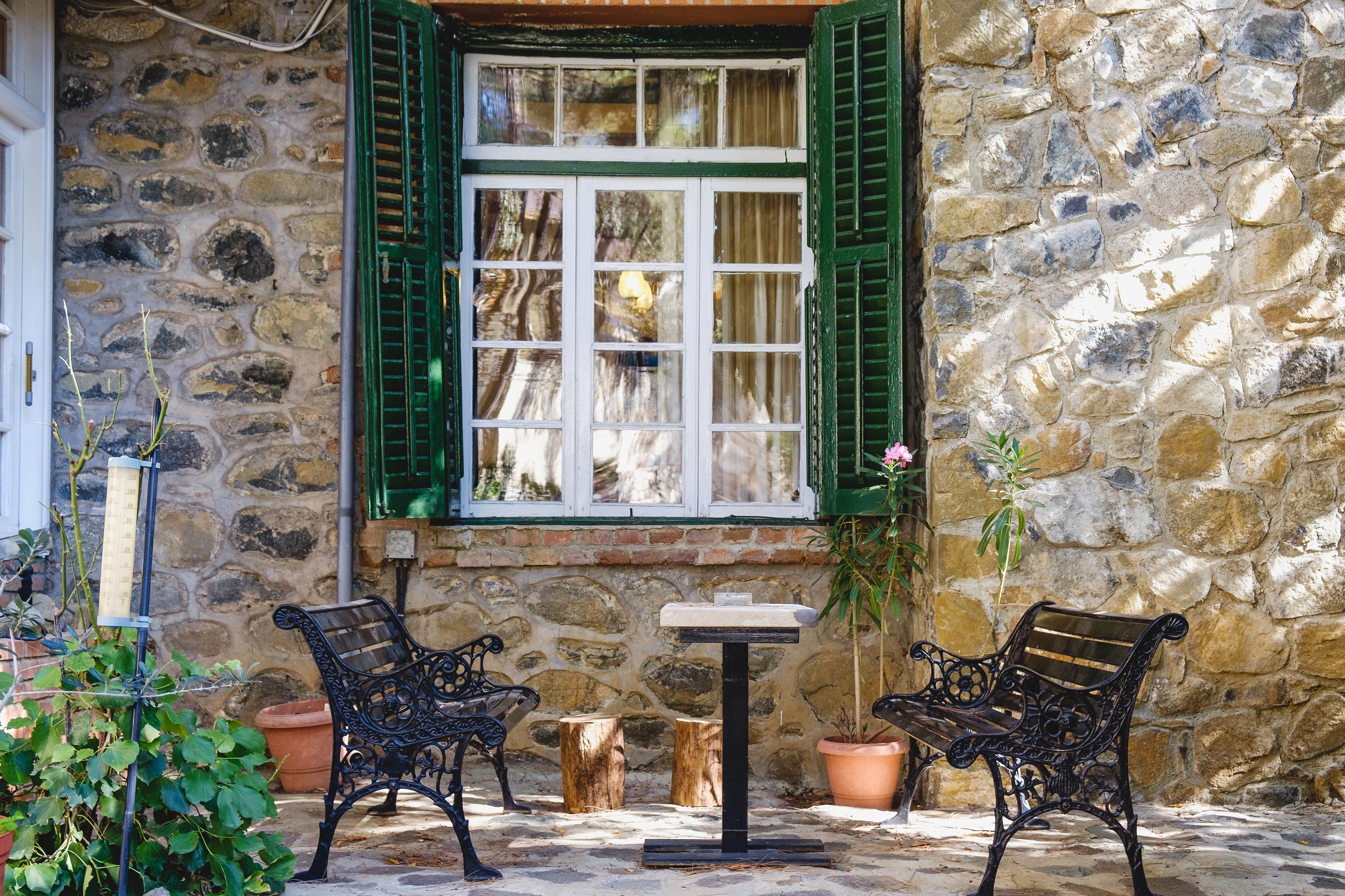 A stone wall with a window, two benches, and potted plants.