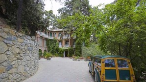 Un muro de piedra, un coche clásico estacionado y un edificio con varias ventanas y balcones.