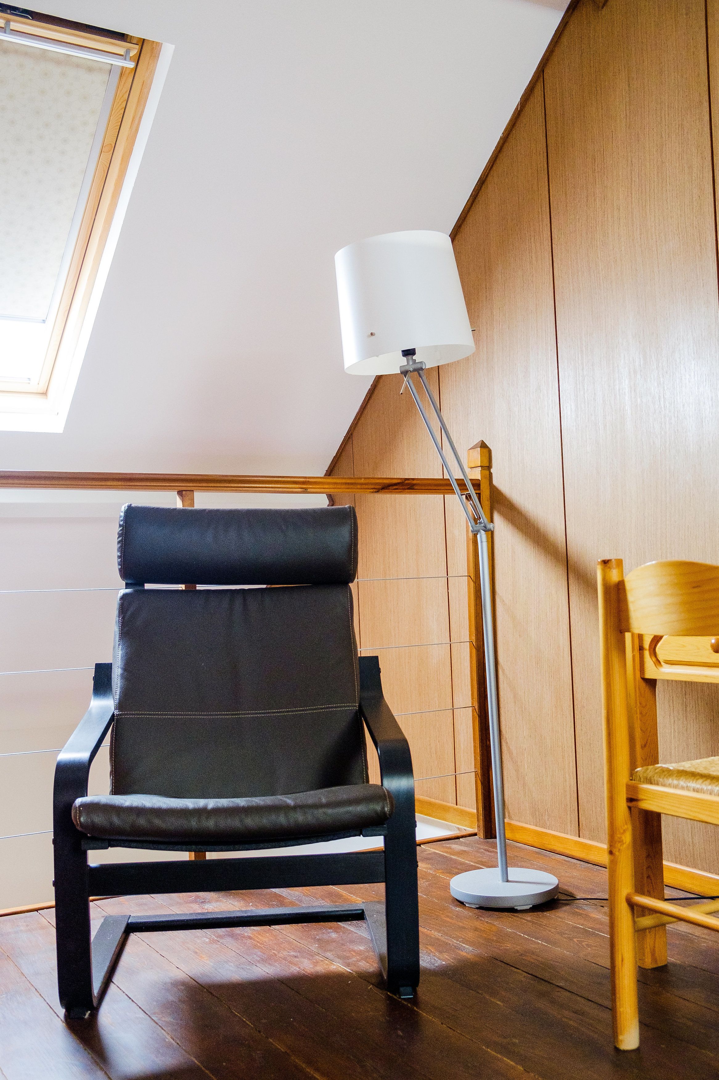 Ein modernes Zimmer mit einem schwarzen Ledersessel, Holzboden und einer weißen Stehlampe.