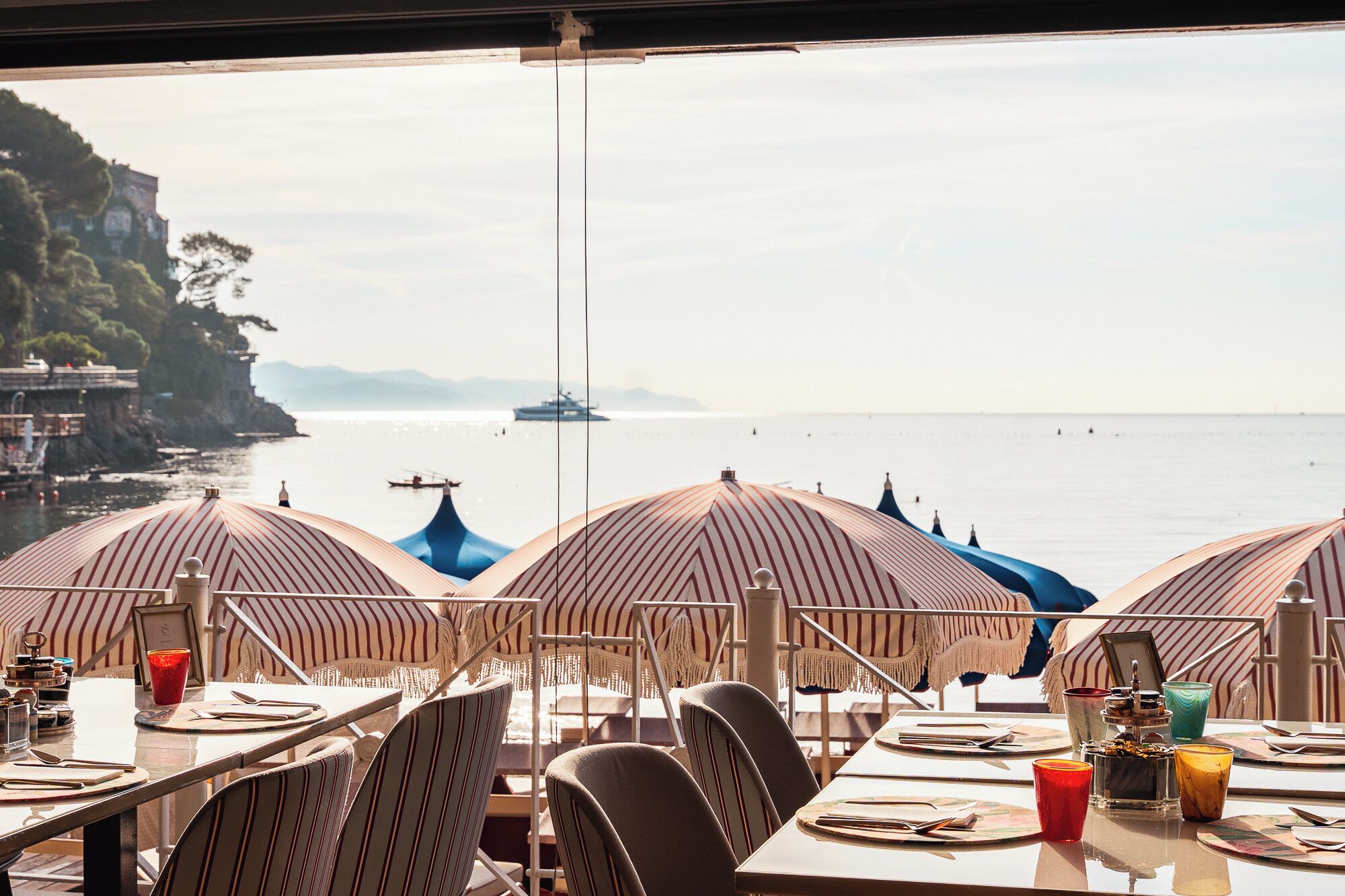 A seaside restaurant with striped umbrellas and tables set for dining, overlooking the ocean.