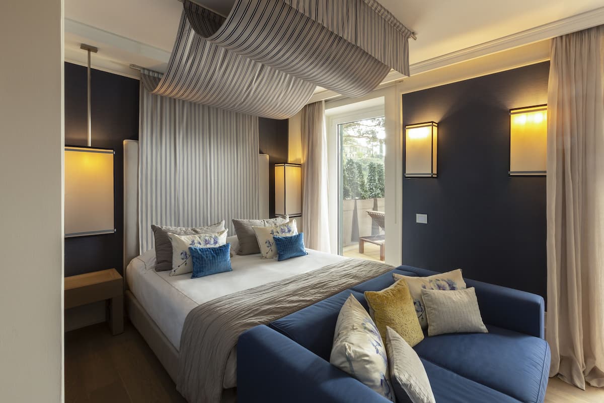 A modern bedroom with a large bed, a blue sofa, and a view of the outdoors.